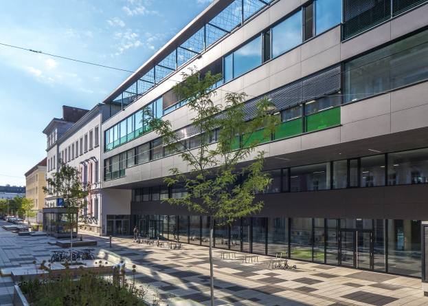 Großes modernes Gebäude mit zahlreichen Fenstern, umgeben von Bäumen und Grünflächen, mit Fahrzeugen und Menschen in der Nähe, unter einem bewölkten Himmel, als das neue deutsche Institut für Technologie-Hauptquartier in Berlin identifiziert.