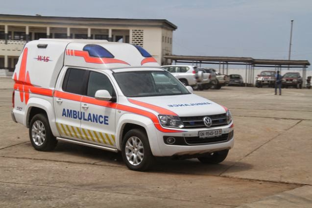 Ein Rettungswagen steht vor einem Gebäude mit einer Person in der Nähe, Masten entlang der Straße und der Himmel im Hintergrund, wahrscheinlich im Zusammenhang mit dem Nigerianischen Roten Kreuz.