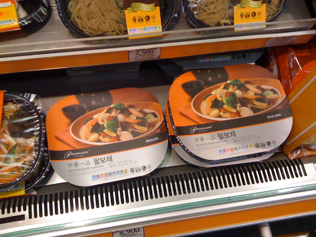 Kisten mit Lebensmitteln auf Regalen mit Preisetiketten.