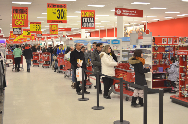 Ein volles Walmart-Geschäft mit Einkaufswagen schiebenden Kunden und Menschen mit Taschen, umgeben von Warenregalen, Schildern und Deckenleuchten.