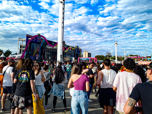 Eine Gruppe von Menschen, einige mit Mützen und Schutzbrillen, steht vor einem Karneval mit Pfählen, Bäumen, Gebäuden und einem bewölkten Himmel im Hintergrund.