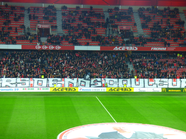 Ein Fußballfeld mit einer großen Menge an Zuschauern auf den Rängen, umgeben von Texttafeln und einem Logo mit Text unten.