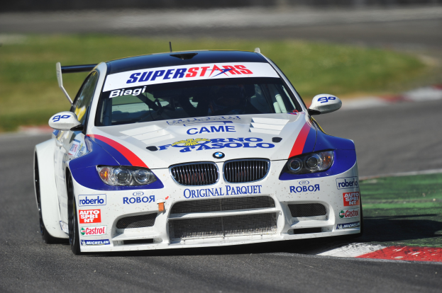 Ein BMW M3 GT3 Rennwagen in Bewegung auf einer Rennstrecke mit unscharfer grüner Hintergrund.