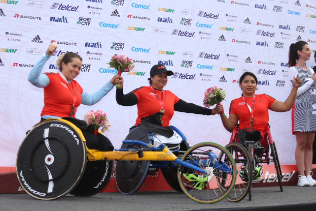 Vier Frauen im Rollstuhl auf einem Podium, jede hält einen Blumenstrauß, mit einem Banner im Hintergrund mit der Aufschrift "Welt-Rollstuhl-Meisterschaften".