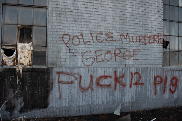 Ein Gebäude mit Graffiti, das "Polizei Mord George Fuck 12 P19" auf der Seite trägt, mit Fenstern und diversen Gegenständen vorne drauf.