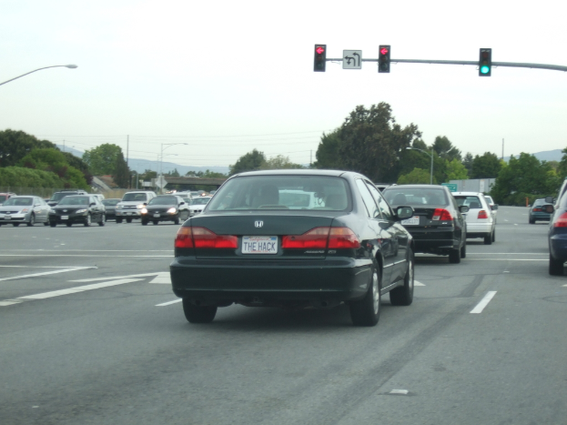 Eine belebte StraÃŸe mit zahlreichen Fahrzeugen, drei StrommÃ¤sten im Hintergrund und einer Ampel auf der rechten Seite unter einem klaren Himmel.