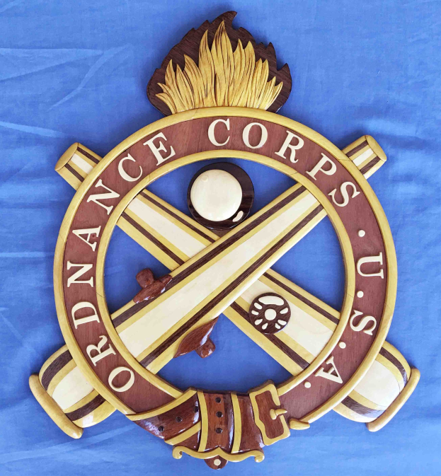 Holzschild mit "Ordnance Corps"-Text, zeigt ein geschnitztes weißes Stern auf navy-Blue-Hintergrund mit goldener Umrandung, montiert auf blauem Tuch in fetter schwarzer Schrift.