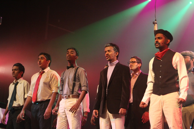 Eine Gruppe von Männern, die ein Drama auf der Bühne spielen, mit grünen Scheinwerfern im Hintergrund.