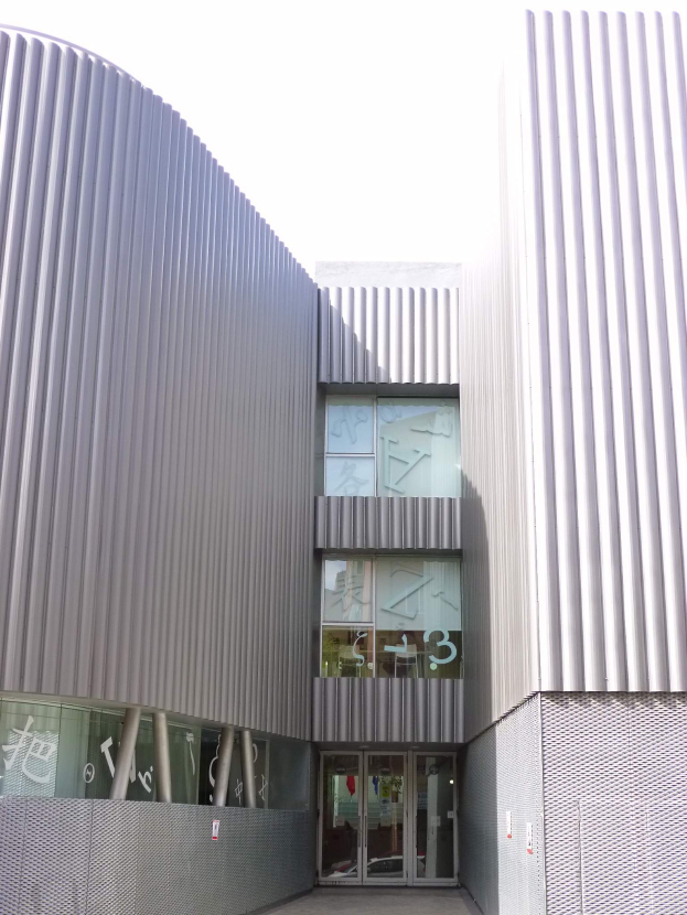 Ein modernes, großes Schulgebäude mit zahlreichen Fenstern und einer Tür, vor einem Hintergrund aus Boden und Himmel.